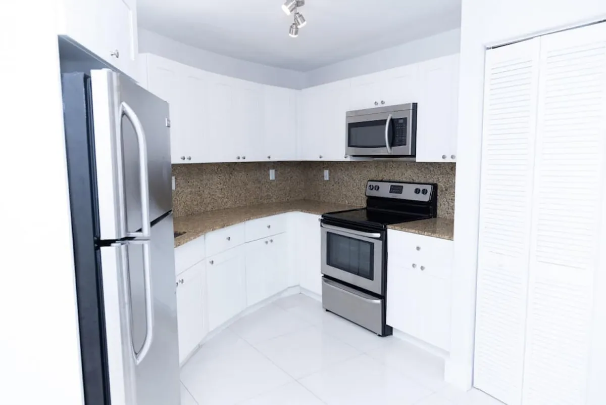 This image zooms in on the modern kitchen area, showcasing stainless steel appliances, a granite countertop, and white cabinetry. The setup is inviting for meal prep and socializing while cooking.